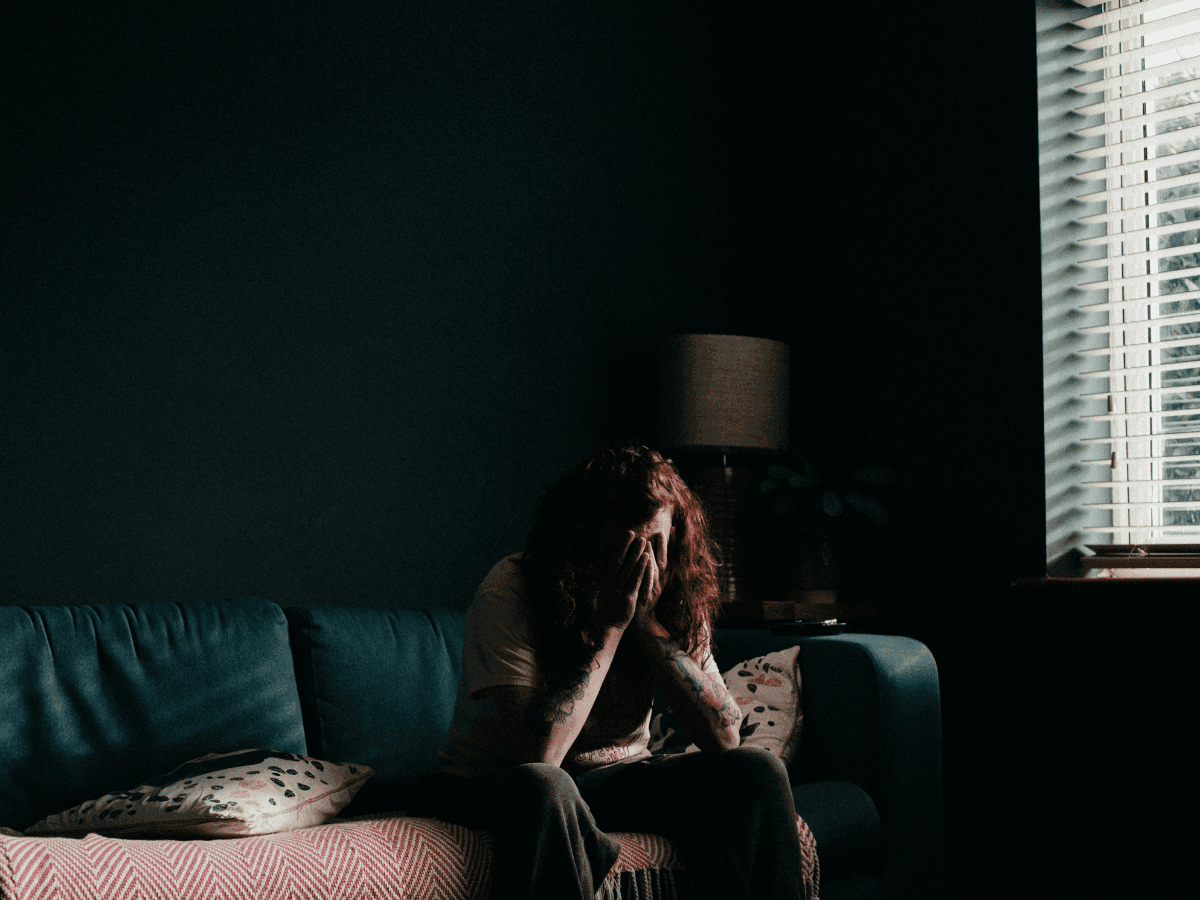 A person with red hair sits on a couch, their face buried in their hands, depicting the struggle with PTSD.